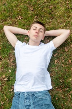 Genç bir çocuk bahar günü çimenlerde kestiriyor.