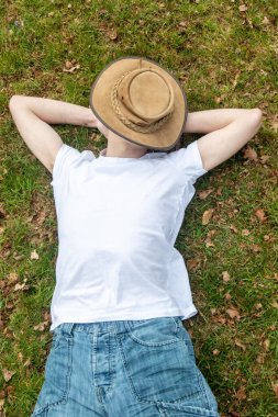 Genç bir çocuk, bahar günü yüzünü kaplayan bir çalılıkla çimenlerde kestiriyor.