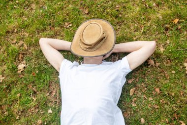 Genç bir çocuk, bahar günü yüzünü kaplayan bir çalılıkla çimenlerde kestiriyor.