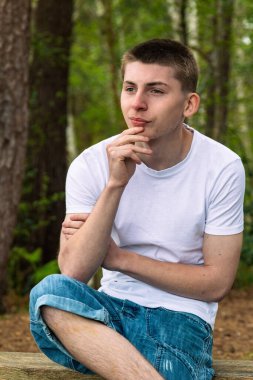 Halka açık bir parkta bankta oturan, beyaz tişört ve mavi kot giyen mutlu ergen çocuk.