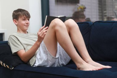 Kanepeye uzanmış roman okuyan bir genç çocuk.