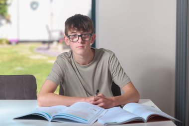 Ergen çocuk mutfak masasında ödev yapıyor ya da düzeltme yapıyor.