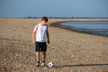 Genç bir çocuk, Stony Beach 'te futbol oynuyor. Sıcak bir Sumemr akşamında.