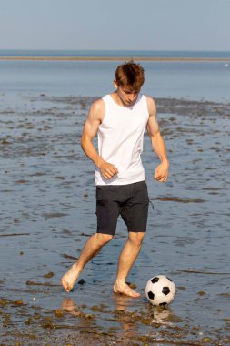 Genç bir çocuk sahilde futbol oynuyor, sıcak bir yaz akşamında..