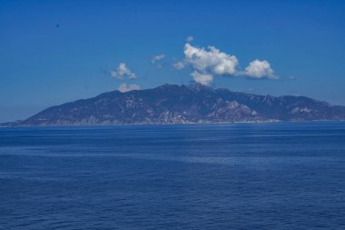 Mavi deniz ve gökyüzü, ufukta bir dağ ve dağın üzerinde beyaz bir bulut. Suda başka bir şey yok, insan yok, gemi yok, sadece manzara yüksek kaliteli bir fotoğraf.