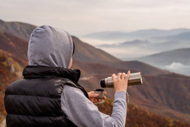 Mutlu bir gezgin kadın, yürüyüş sırasında dinlenmek için termos şişesinden kahve ya da çay içer ve dağlardaki macera yolculuğunun tadını çıkarır. Yüksek kalite fotoğraf