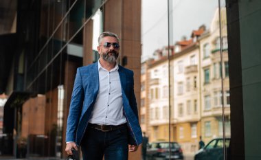 Yakışıklı yaşlı bir iş adamı ofis binasının yanındaki caddede yürüyor. Yüksek kalite fotoğraf