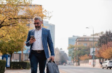 Yakışıklı, olgun bir iş adamı sokakta yürürken cep telefonu uygulaması kullanıyor. Yüksek kalite fotoğraf