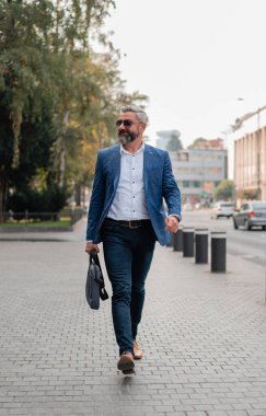 Yakışıklı, olgun bir iş adamı şehir caddesinde yürüyor. h