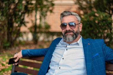 Yakışıklı, olgun bir iş adamı parkta bankta otururken dinleniyor. - Evet. Yüksek kalite fotoğraf