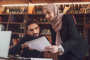 Modern ofiste proje planlama stratejisi üzerinde çalışan genç bir erkek ve Müslüman kadından oluşan bir iş ekibi veya üniversite kampüsündeki kütüphanede birlikte çalışan Arap üniversite öğrencileri.
