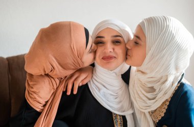 Mutlu Müslüman bir aile, anneler ve iki kız çocuğu anneler gününde anneler gününde birbirlerine bağlanmak için kanepede sevgiyle sarılıp gülümsüyorlar. Yüksek kalite fotoğraf