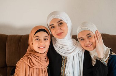 Evde mutlu bir Müslüman ailenin portresi, tesettürlü genç bir anne ve iki çocuk anne kameraya bakıyor ve Anneler Günü 'nde gülümsüyor. Yüksek kalite fotoğraf