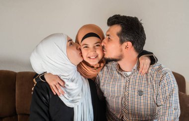 Mutlu Müslüman bir aile, genç bir anne ve baba tesettüre bakıp gülümseyen güzel bir kızı öpüyor. Yüksek kalite fotoğraf
