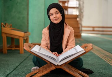 A happy child girl reading a holy book Quran inside the mosque. . High quality photo clipart