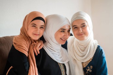 Evde mutlu bir Müslüman ailenin portresi, tesettürlü genç bir anne ve iki çocuk anne kameraya bakıyor ve Anneler Günü 'nde gülümsüyor. Yüksek kalite fotoğraf