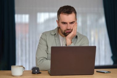 Fazla mesai yapan sıkıcı bir adam, dizüstü bilgisayarın önünde oturuyor ve ekrana bakmaktan rahatsız oluyor. Yüksek kalite fotoğraf