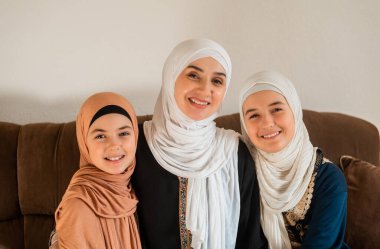 Evde mutlu bir Müslüman ailenin portresi, tesettürlü genç bir anne ve iki çocuk anne kameraya bakıyor ve Anneler Günü 'nde gülümsüyor. Yüksek kalite fotoğraf