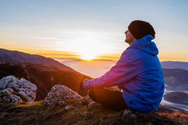 Huzurlu bir adam yoga yapıyor, doğa manzaralı bir dağın tepesinde tek başına dinleniyor. Yüksek kalite fotoğraf