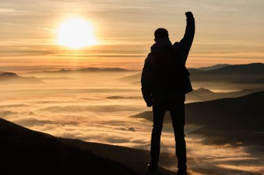 Güneşin doğuşunda ya da batışında bir dağın tepesinde başarıyı kutlayan bir insan silueti. Yüksek kalite fotoğraf