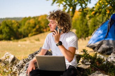 Telefonla konuşan ve dışarıda dizüstü bilgisayar kullanan genç ve mutlu bir adam. Yüksek kalite fotoğraf