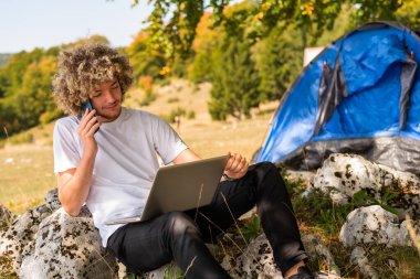 Telefonla konuşan ve dışarıda dizüstü bilgisayar kullanan genç ve mutlu bir adam. Yüksek kalite fotoğraf