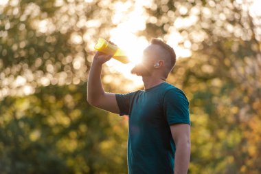 Koşudan sonra şişeden su içen sportif bir genç adam ya da yaz parkında spor yapan sağlıklı bir yaşam tarzı. Yüksek kalite fotoğraf