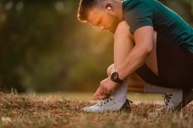 Koşu ayakkabılarını kablosuz kulaklıkla bağlayan genç bir atletik parkta koşuya ya da antrenmana hazırlanmak için müzik dinliyor, aktif bir yaşam tarzı. Yüksek kalite fotoğraf