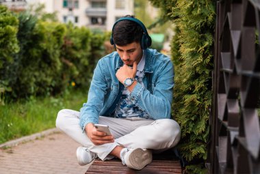 Dışarıda cep telefonu kullanan kulaklıklı genç bir adam. Yüksek kalite fotoğraf