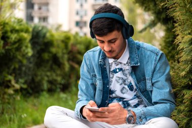 Kulaklıklı, dışarıda cep telefonu kullanan genç ve mutlu bir adam. Yüksek kalite fotoğraf