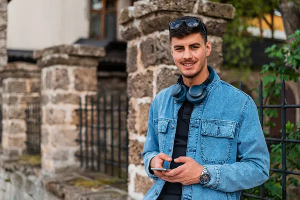 Şehirde cep telefonu kullanan genç ve mutlu bir adam kameraya bakıyor ve gülümsüyor. Yüksek kalite fotoğraf