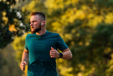 Genç atletik bir adam parkta koşuyor ya da koşuyor kablosuz kulaklıkla sağlıklı yaşam tarzını dinliyor. Yüksek kalite fotoğraf