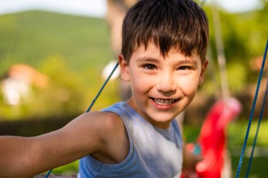 Mutlu bir Asyalı çocuk yaz bahçesinde salıncakta sallanıyor kameraya bakıyor ve gülümsüyor. Yüksek kalite fotoğraf