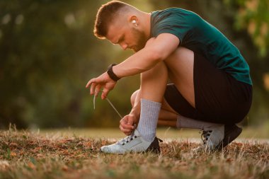 Koşu ayakkabılarını kablosuz kulaklıklarla bağlayan genç bir atletik parkta aktif bir yaşam tarzına hazırlanmak için motivasyon müziği dinliyor. Yüksek kalite fotoğraf