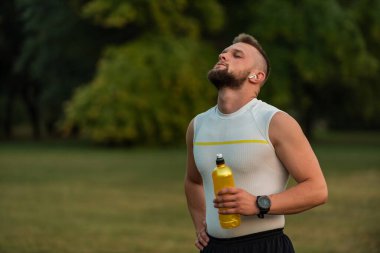 Gözleri kapalı, kablosuz kulaklıkla müzik dinleyen ve parkta koşudan ya da antrenmandan sonra dinlenen sağlıklı, genç bir adam. Yüksek kalite fotoğraf