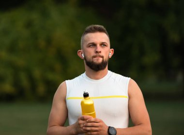 Genç, zinde bir adam kablosuz kulaklıklardan müzik dinler ve bir yaz parkında spor yaptıktan sonra dinlenir. Aktif ve sağlıklı bir yaşam tarzı sergiler. Yüksek kalite fotoğraf