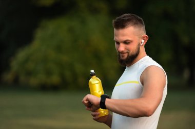 Mutlu atletik adam parkta koşarken ya da koşarken kalp atışlarını kontrol ediyor. Aktif ve sağlıklı yaşam tarzı, fitness ve açık hava egzersiz konsepti. Yüksek kalite fotoğraf