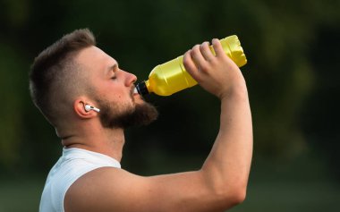 Gözleri kapalı, kablosuz kulaklıkla müzik dinleyen, su içen ya da parkta koşudan ya da antrenmandan sonra beslenme suyu içen genç bir adam. Aktif, sağlıklı bir yaşam tarzı. Yüksek kalite