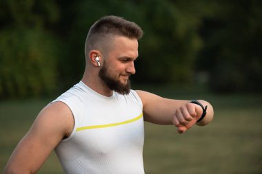 Mutlu atletik adam parkta koşarken ya da koşarken kalp atışlarını kontrol ediyor. Aktif ve sağlıklı yaşam tarzı, fitness ve açık hava egzersiz konsepti. Yüksek kalite fotoğraf