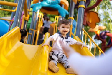 Mutlu bir çocuk ailesiyle birlikte bir yaz parkında kaydırağın üzerinde oynuyor. Yüksek kalite fotoğraf
