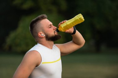 Gözleri kapalı, kablosuz kulaklıkla müzik dinleyen, su içen ya da parkta koşudan ya da antrenmandan sonra beslenme suyu içen genç bir adam. Aktif, sağlıklı bir yaşam tarzı. Yüksek kalite