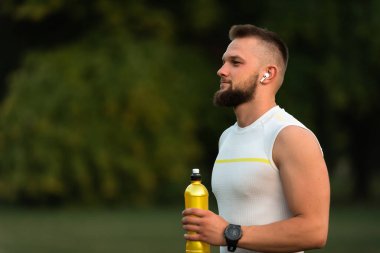 Genç, zinde bir adam, kablosuz kulaklıklarla müzik dinler ve bir yaz parkında çalıştıktan sonra dinlenir. Aktif ve sağlıklı bir yaşam tarzı sergilerler. Yüksek kalite fotoğraf