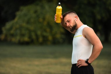 Yorgun erkek sporcu ya da formda bir adam spor yaptıktan sonra su şişesiyle serinliyor ya da parkta koşuyor. Aktif yaşam tarzı. Yüksek kalite fotoğraf