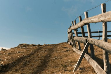 Açık mavi gökyüzünün altındaki tepelik arazide ahşap çitleri olan kırsal bir arazi. Sıcak öğleden sonra ışığında çekilen huzurlu doğal manzara. Yüksek kalite fotoğraf