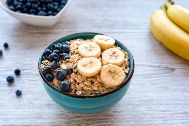 Taze meyveli yulaf ezmesi, yulaflı, muzlu ve yaban mersinli sağlıklı bir kahvaltı kasesi ve ahşap bir masada yaban mersini. Yüksek kalite fotoğraf