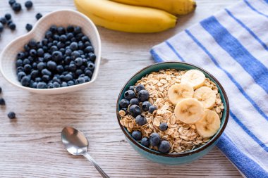 Taze meyveli yulaf ezmesi, yulaflı, muzlu ve yaban mersinli sağlıklı bir kahvaltı kasesi ve ahşap bir masada yaban mersini. Yüksek kalite fotoğraf