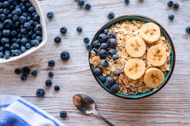 Taze meyveli yulaf lapası, yulaflı, muzlu ve yaban mersinli sağlıklı kahvaltı kasesi ve ahşap bir masada yaban mersini. Yüksek kalite fotoğraf