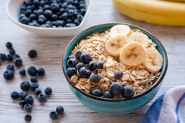 Taze meyveli yulaf ezmesi, yulaflı, muzlu ve yaban mersinli sağlıklı bir kahvaltı kasesi ve ahşap bir masada yaban mersini. Yüksek kalite fotoğraf