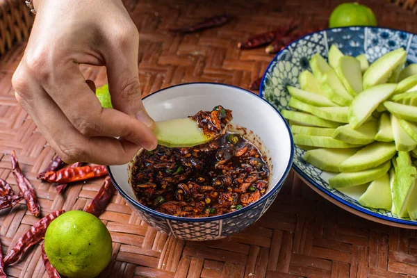 Mangoları tatlı balık sosuna batıran bir el. Tatlı balık soslu yeşil mango Tayland 'da en sevilen yemektir..