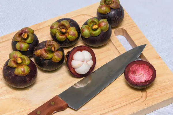 Meyve kraliçesi. Ahşap tabakta mangosen ve bıçak.